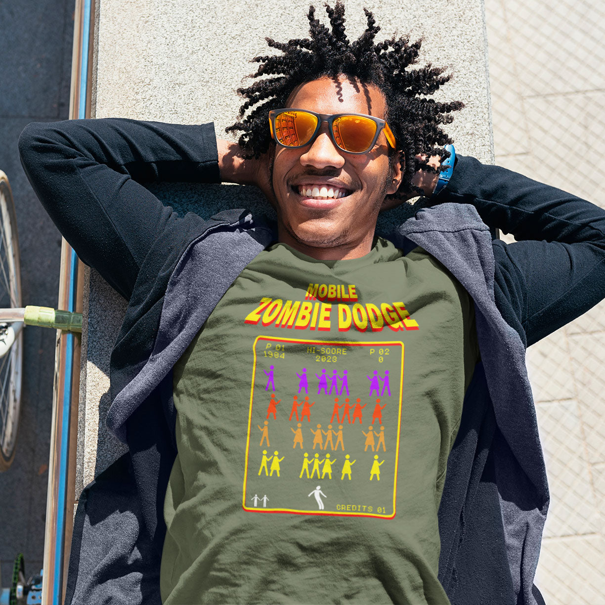 Person wearing a green t-shirt with a graphic design, standing outdoors. A satirical gamer t-shirt design for anyone who feels they are in a repetitive 80's video game every time they enter a crowded street scene. Welcome to the age of the mobile phone and lack of social awareness. Made from 100% organic ring-spun cotton, this unisex gamer t-shirt is alternative and original. It's high-quality, super comfy, and best of all—eco-friendly.