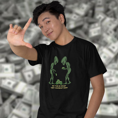 Person wearing a black t-shirt with green alien design in front of a background of money. This funny alien t shirt is for alien lovers, and depicts the disappointment of a civilisation now overly obsessed with money and greed. Is it any wonder the aliens have given up on us. Made from 100% organic ring-spun cotton, this anti capitalist t shirt is unisex, high-quality, super comfy, and best of all, eco-friendly.