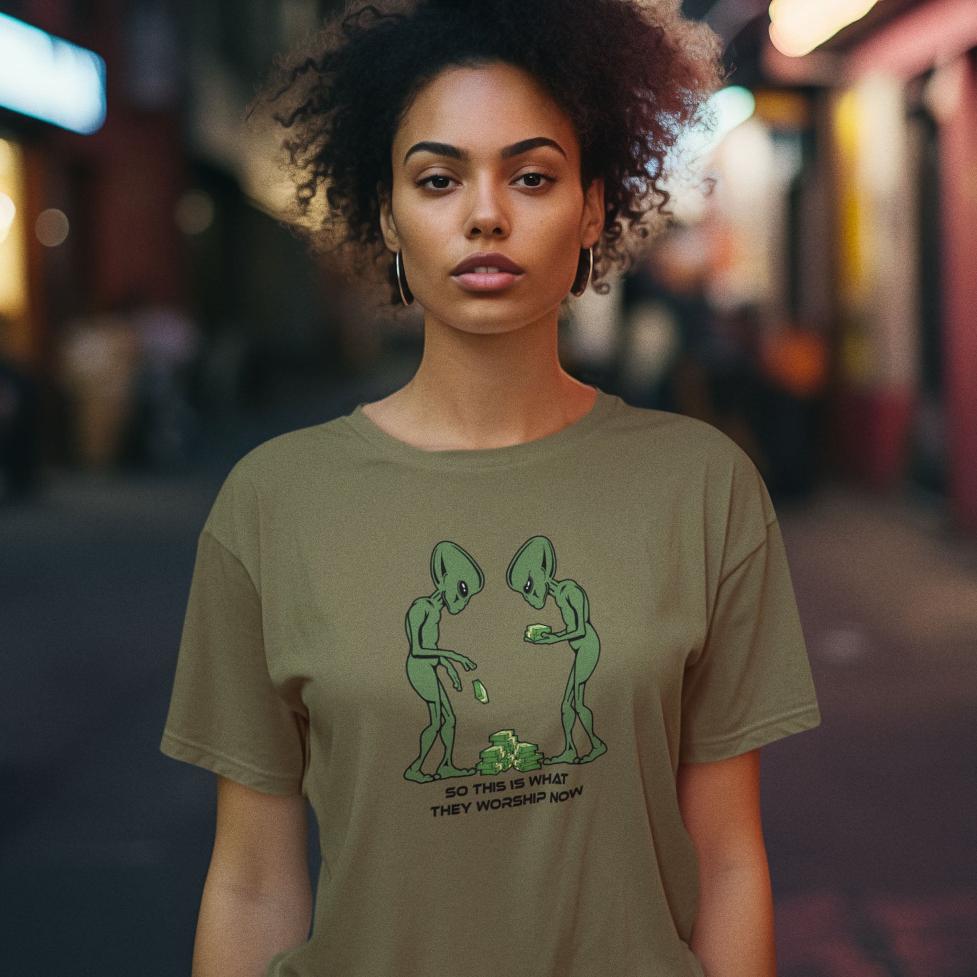 Woman wearing a green t-shirt with a graphic design on a blurred street background. This funny anti-capitalism t-shirt is for alien lovers, and depicts the disappointment of a civilisation now overly obsessed with money and greed. Is it any wonder the aliens have given up on us. Made from 100% organic ring-spun cotton, this social awareness/alien t-shirt is unisex, high-quality, super comfy, and best of all, eco-friendly.