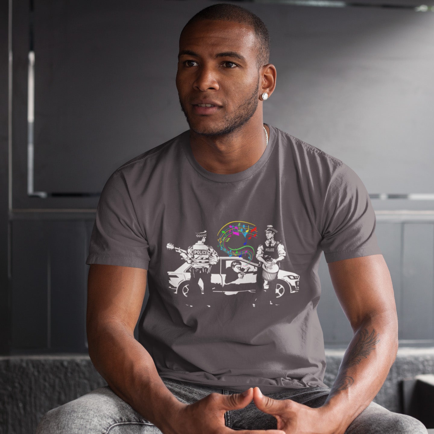 Man wearing an anthracite t-shirt with a graphic design sitting in a room. A witty stencil graffiti t shirt design depicting an alternative reality. We can only dream of the day the police pull you over to try out a new tune on the breathalyser. This is an urban art t shirt for people who think outside the box. Made from 100% organic ring-spun cotton, this funny stencil graffiti t shirt is unisex, high-quality, super comfy, and best of all, eco-friendly.