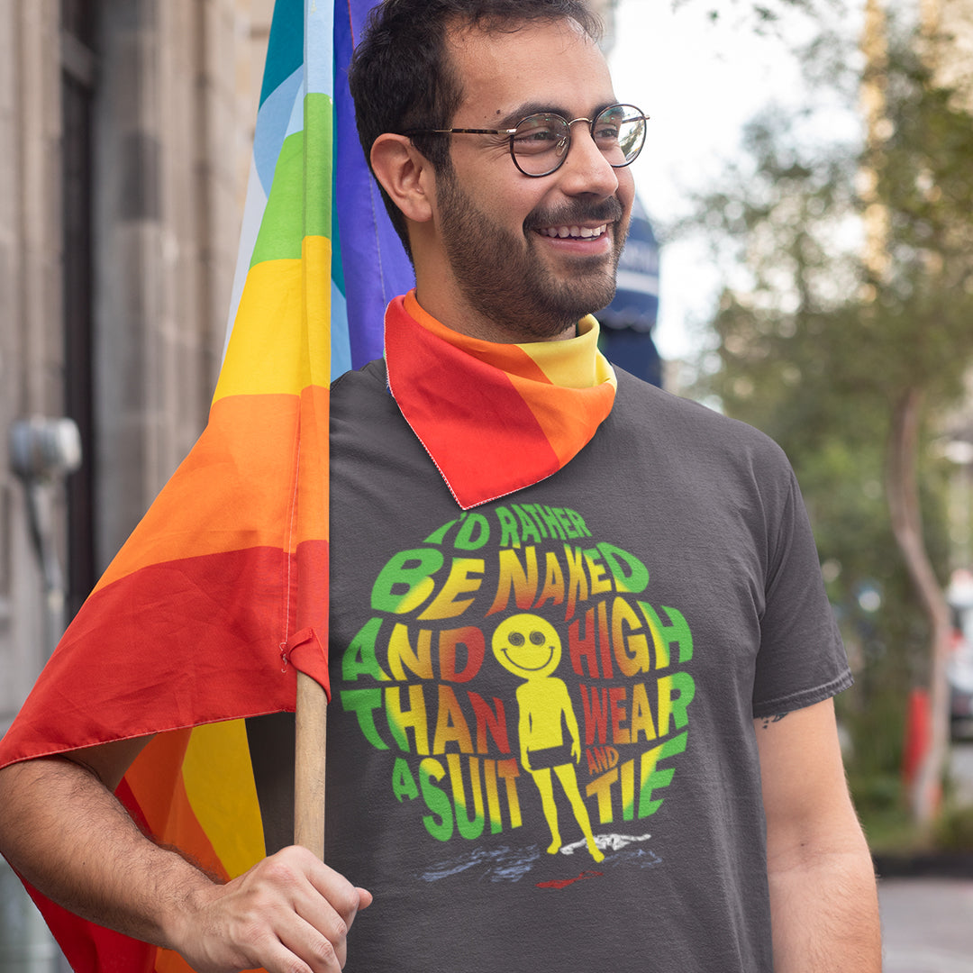 A man wearing glasses and a dark gray graphic t-shirt with a rainbow bandana around his neck, holding a rainbow pride flag outdoors.