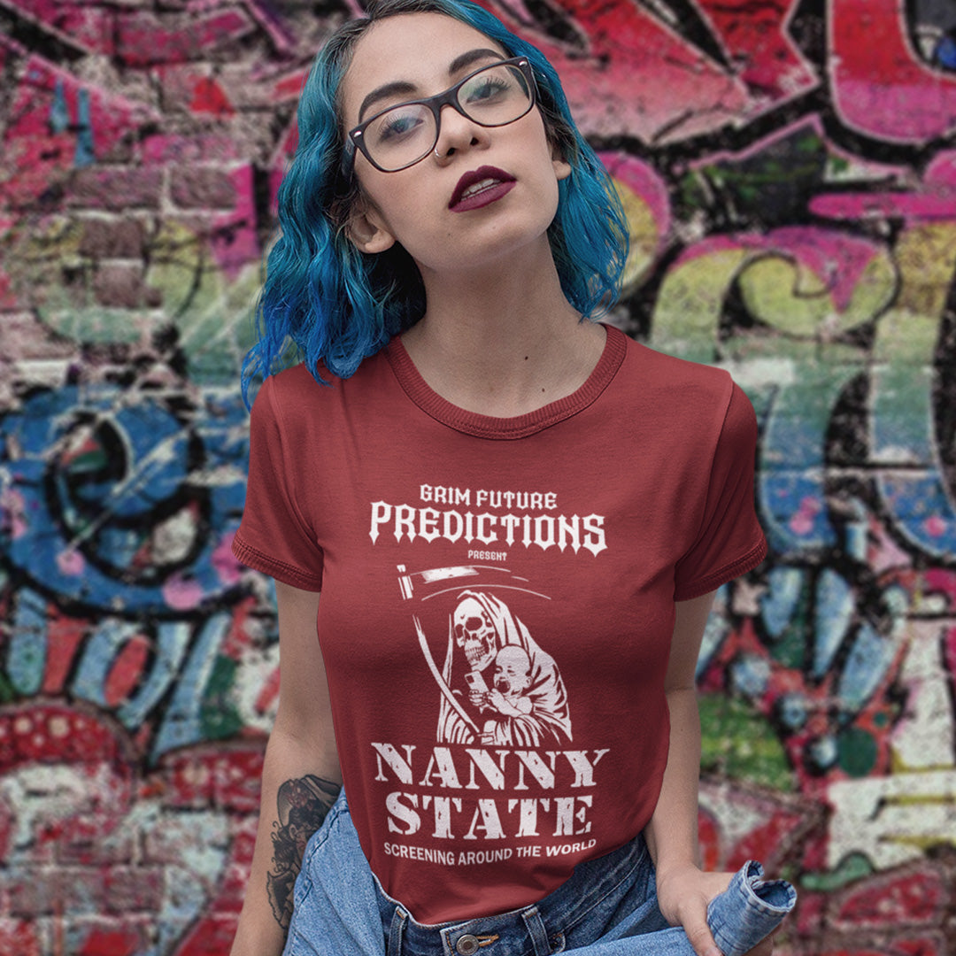 A woman with bright blue hair and glasses wearing a maroon graphic t-shirt that reads 'GRIM FUTURE PREDICTIONS PRESENT NANNY STATE SCREENING AROUND THE WORLD' with a grim reaper illustration, posed in front of a colorful graffiti wall.