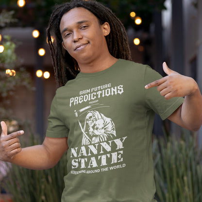 A man wearing an olive green graphic t-shirt with a white print that reads 'GRIM FUTURE PREDICTIONS PRESENTS NANNY STATE SCREENING AROUND THE WORLD' alongside an illustration of a nurse and a baby. He is posing outdoors with blurred lights and plants in the background.