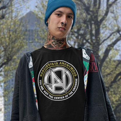 Person wearing a black t-shirt with 'Narcissists Anonymous' logo and text, standing outdoors. A satirical counter culture t shirt design suggesting narcissism is an illness in need of treatment. Wouldn't it be good if there was a place narcissists could go to get therapy and support for their disease. Made from 100% organic ring-spun cotton, this emotional intelligence t-shirt is unisex, high-quality, super comfy, and best of all, eco-friendly.