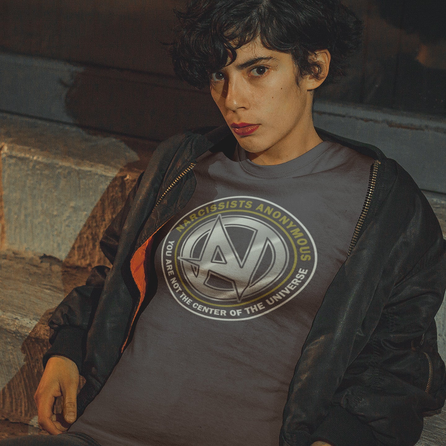 Person wearing a t-shirt with a logo and text, sitting against a stone wall. A satirical t-shirt design suggesting narcissism is an illness in need of treatment. Wouldn't it be good if there was a place narcissists could go to get therapy and support for their disease. Made from 100% organic ring-spun cotton, this emotional intelligence t-shirt is unisex, high-quality, super comfy, and best of all, eco-friendly.