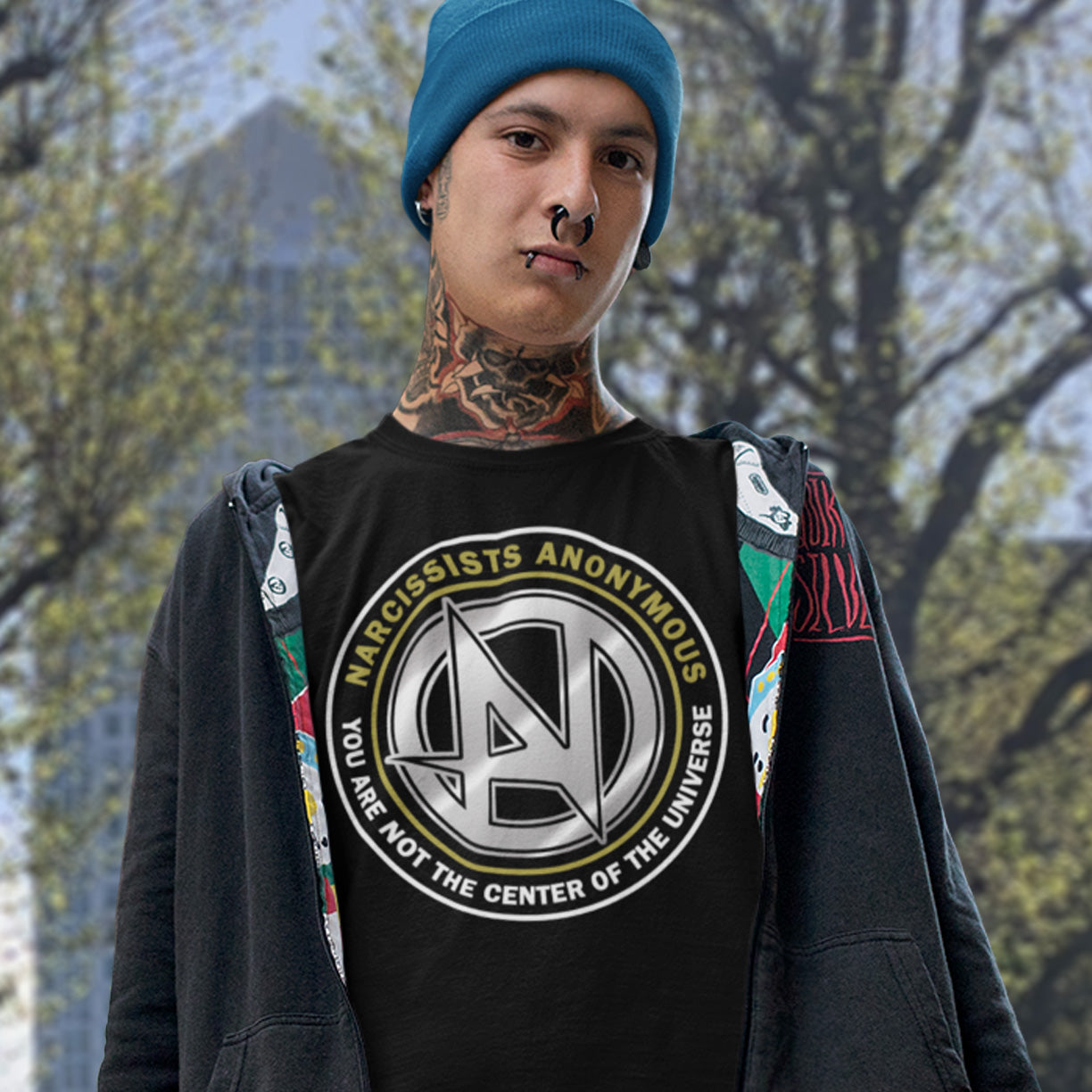 Person wearing a black t-shirt with a logo and text, standing outdoors with trees in the background. A satirical t-shirt design suggesting narcissism is an illness in need of treatment. Wouldn't it be good if there was a place narcissists could go to get therapy and support for their disease. Made from 100% organic ring-spun cotton, this emotional intelligence t-shirt is unisex, high-quality, super comfy, and best of all, eco-friendly.