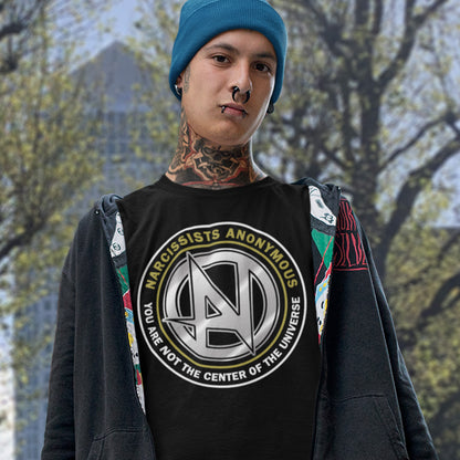 Person wearing a black t-shirt with a logo and text, standing outdoors with trees in the background. A satirical t-shirt design suggesting narcissism is an illness in need of treatment. Wouldn't it be good if there was a place narcissists could go to get therapy and support for their disease. Made from 100% organic ring-spun cotton, this emotional intelligence t-shirt is unisex, high-quality, super comfy, and best of all, eco-friendly.