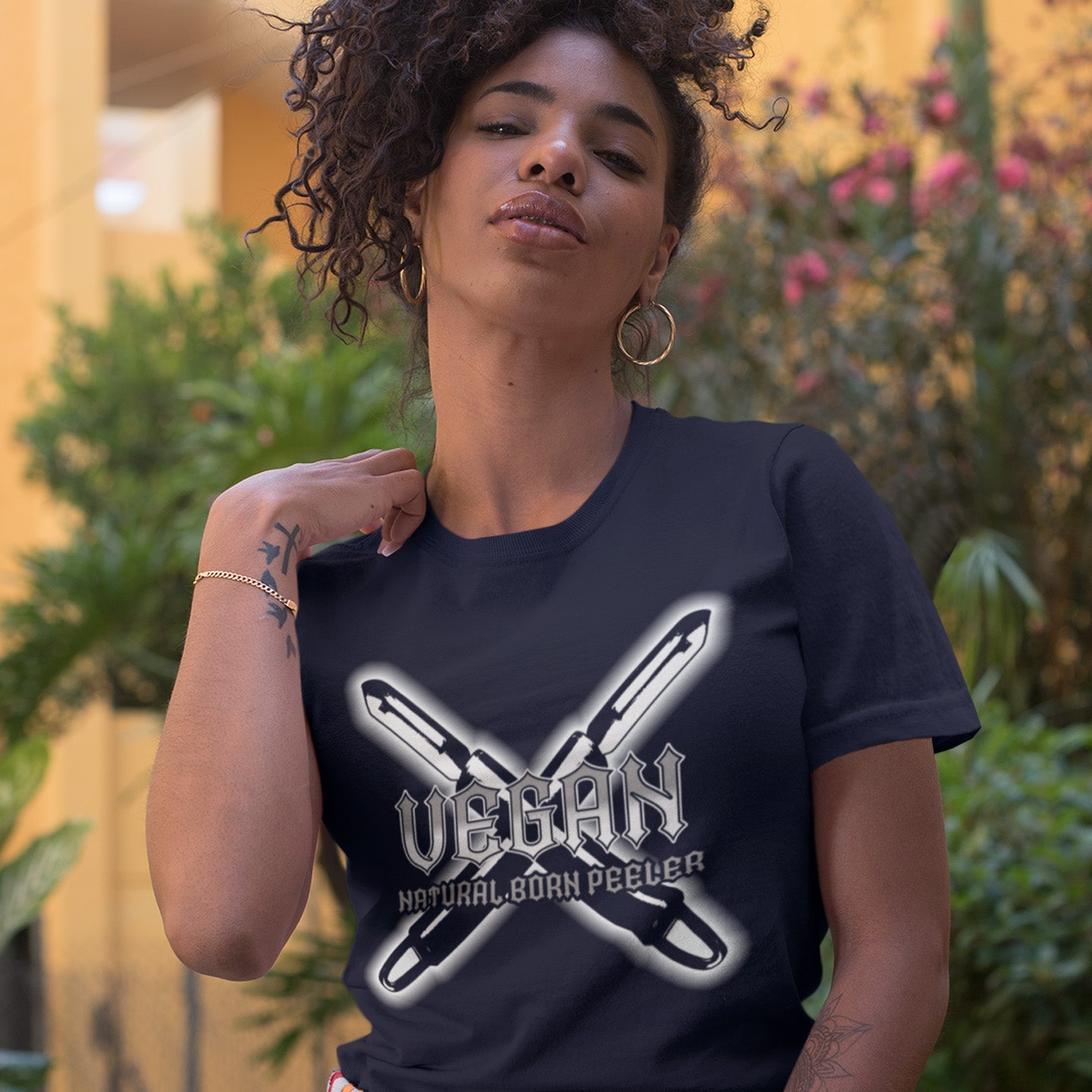 Woman wearing a French navy t-shirt with 'Vegan' and 'Natural Born Peeler' text, standing outdoors. A funny vegan t-shirt with menace. A tribute to the number one weapon of choice for a planet lover. A unique dairy free design for all plant based warriors. Made from 100% organic ring-spun cotton, this vegan t-shirt is unisex, high-quality, super comfy, and best of all, eco-friendly.