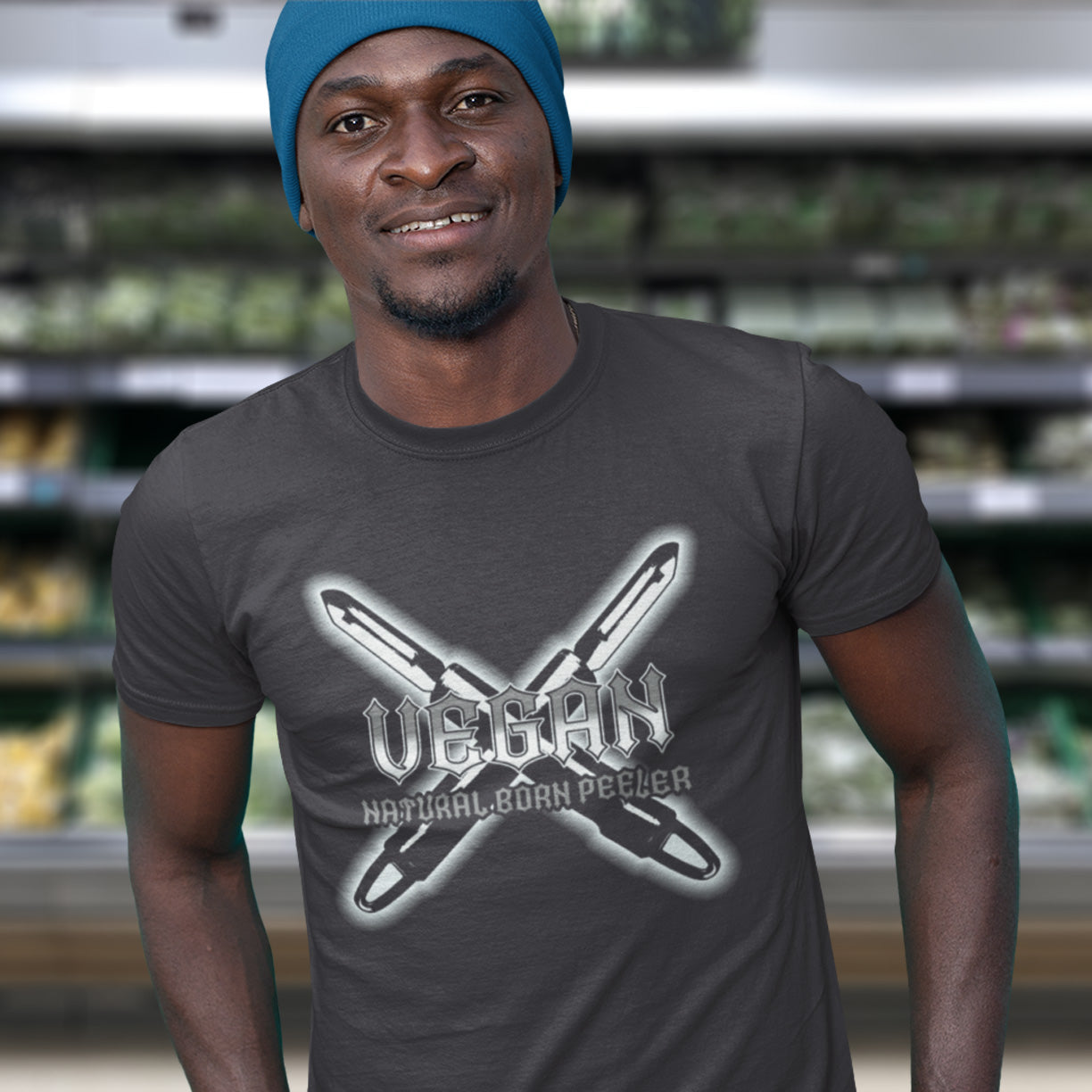 Man wearing an anthracite t-shirt with 'Vegan Natural Born Peeler' design in a grocery store setting. A funny vegan t-shirt with menace. A tribute to the number one weapon of choice for a planet lover. A unique dairy free design for all plant based warriors. Made from 100% organic ring-spun cotton, this vegan t-shirt is unisex, high-quality, super comfy, and best of all, eco-friendly.