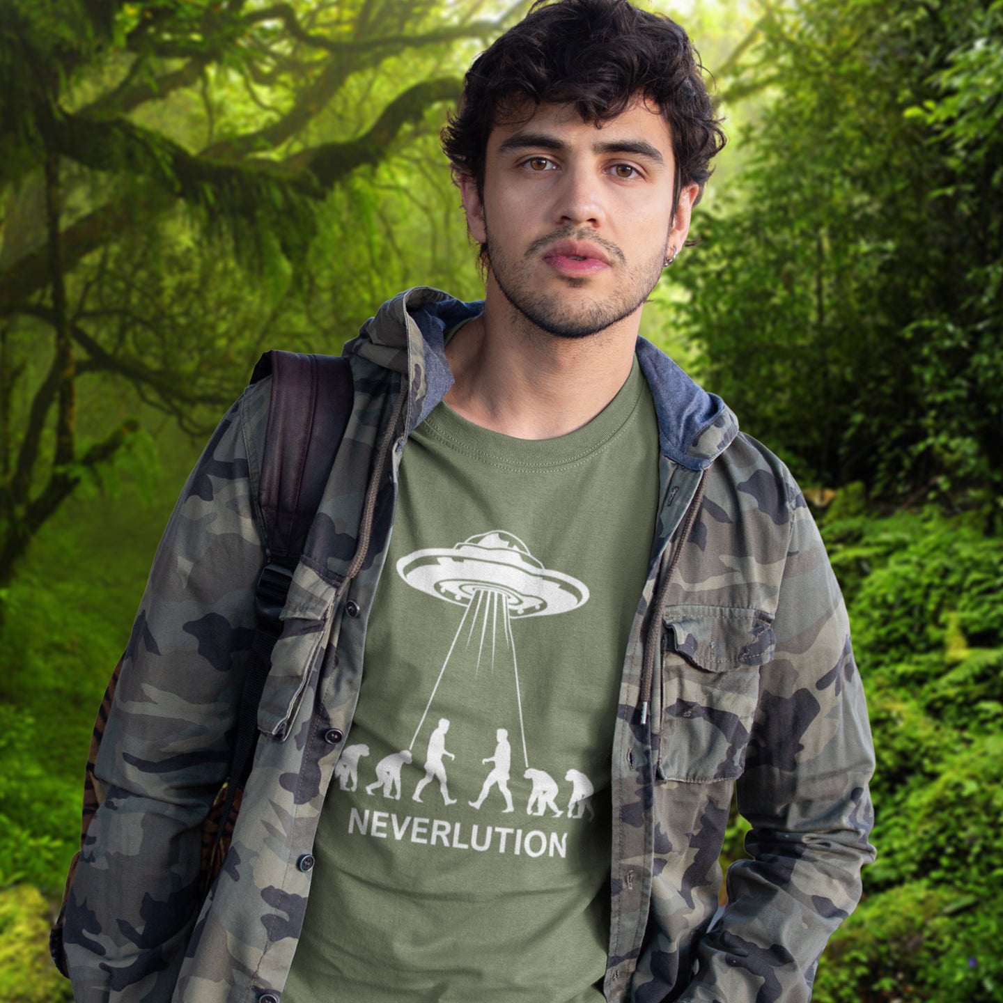 Man wearing a khaki t-shirt with 'Neverlution' design in a forest setting. An alien conspiracy theory t-shirt suggesting a different path of our evolution. Did evolution never really happen the way we are told, or is there a more intergalactic and colourful answer ? Made from 100% organic ring-spun cotton, this conspiracy theory t-shirt is unisex, high-quality, super comfy, and best of all, eco-friendly.