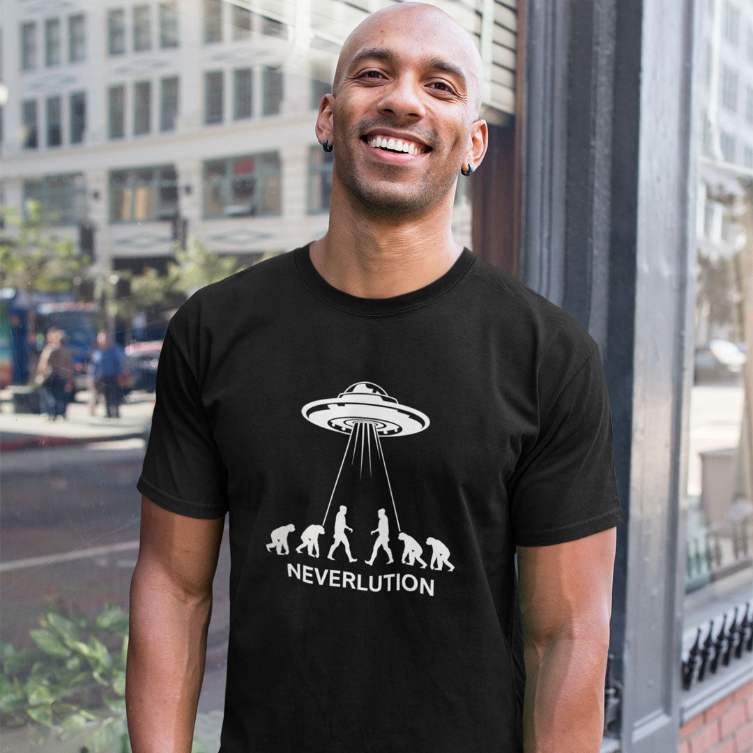 A smiling man wearing a black graphic t-shirt with a white print of a UFO and the word 'NEVERLUTION' on the front, standing outdoors in front of a city building.