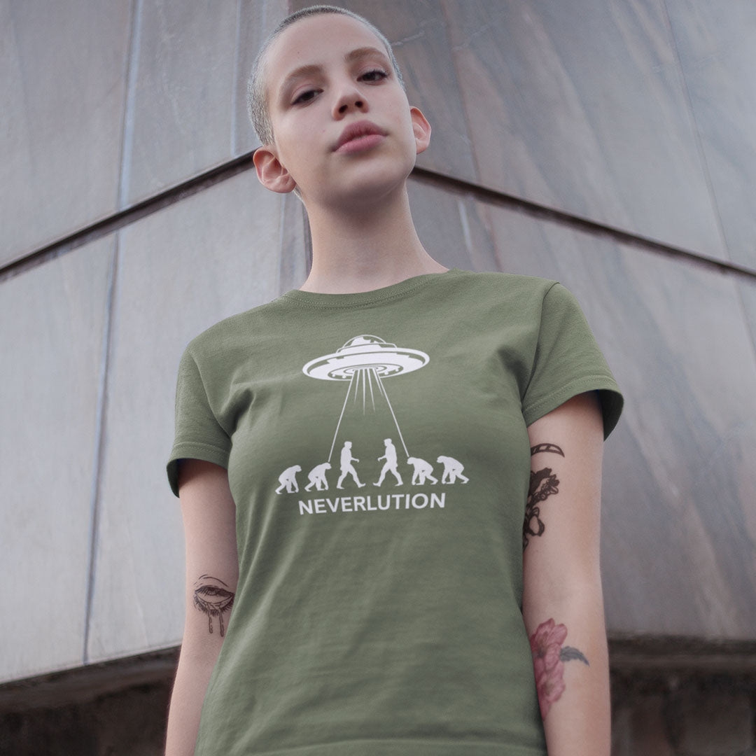 A person wearing an olive green graphic t-shirt with a white UFO and ape evolution design that spells 'NEVERLUTION'. The background is a gray concrete wall.