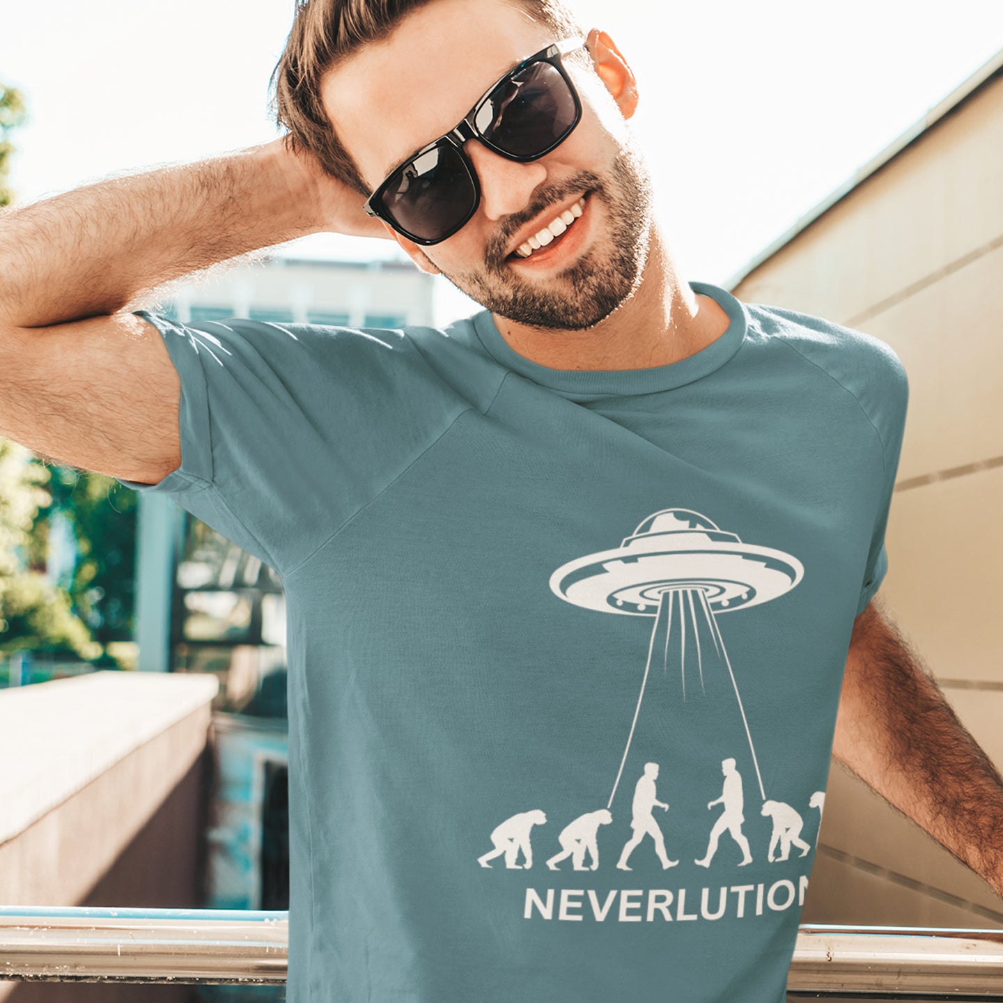 Man wearing a t-shirt with a UFO and evolution graphic, text 'NEVERLUTION'. An alien conspiracy theory t-shirt suggesting a different path of our evolution. Did evolution never really happen the way we are told, or is there a more intergalactic and colourful answer ? Made from 100% organic ring-spun cotton, this conspiracy theory t-shirt is unisex, high-quality, super comfy, and best of all, eco-friendly.