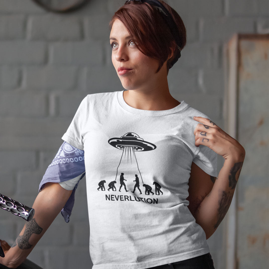A woman wearing a white graphic t-shirt with a black print of an alien UFO and the word 'NEVERLUTION' next to an evolution sequence. She has a purple bandana tied around her arm and is posing in front of a gray brick wall.