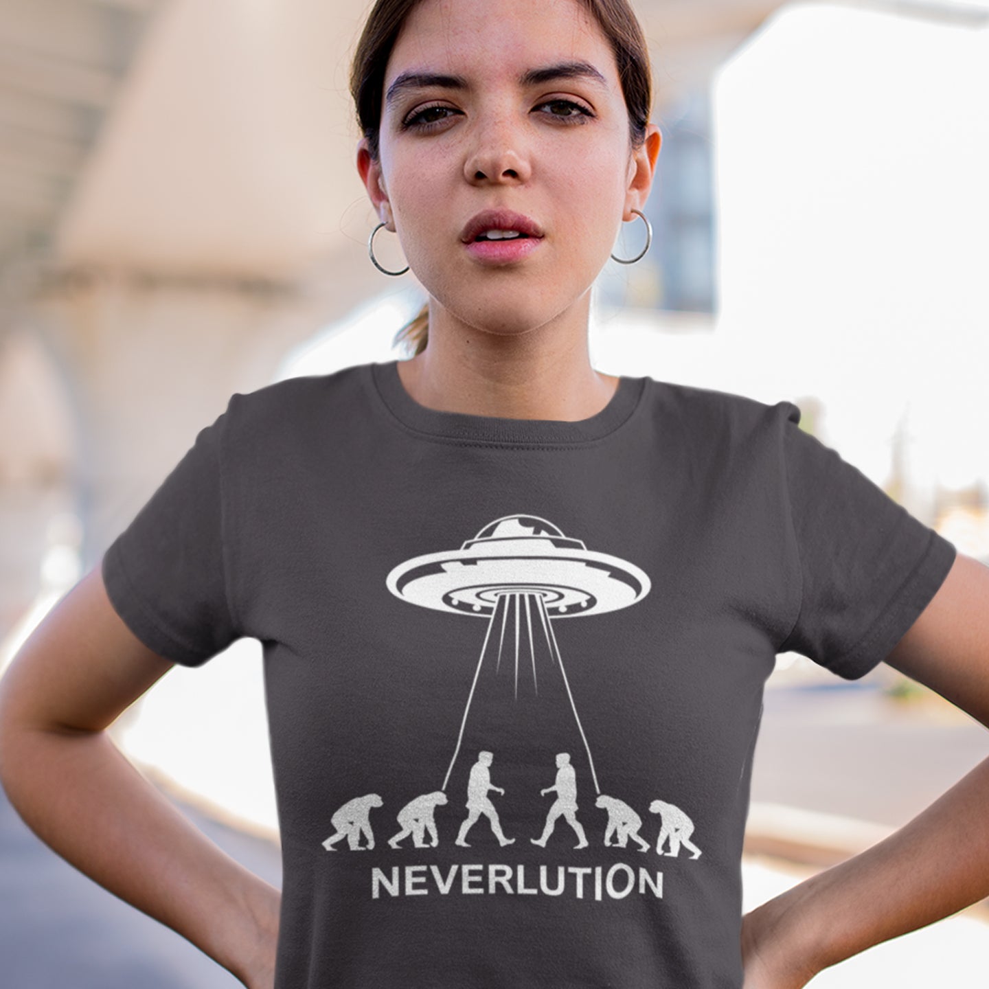 Person wearing a t-shirt with a UFO and evolution graphic and 'NEVERLUTION' text. An alien conspiracy theory t-shirt suggesting a different path of our evolution. Did evolution never really happen the way we are told, or is there a more intergalactic and colourful answer ? Made from 100% organic ring-spun cotton, this conspiracy theory t-shirt is unisex, high-quality, super comfy, and best of all, eco-friendly.