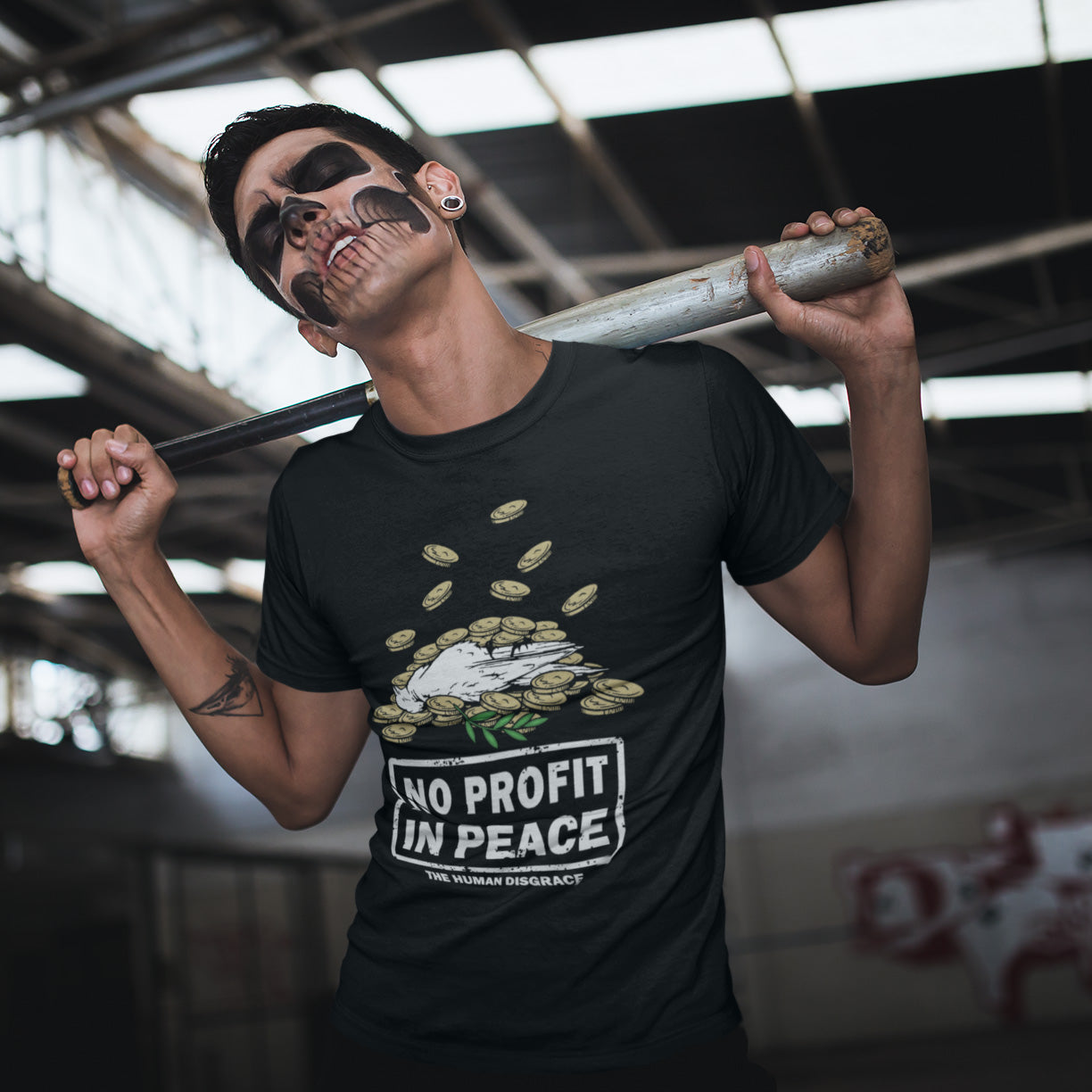 Person wearing a black t-shirt with 'No Profit in Peace' graphic, holding a baseball bat. An anti-war t-shirt exposing the true reason for war. A cynical view of why peace has never really been an option and what big business war has always been. Made from 100% organic ring-spun cotton, this political t-shirt is unisex, high-quality, super comfy, and best of all, eco-friendly.