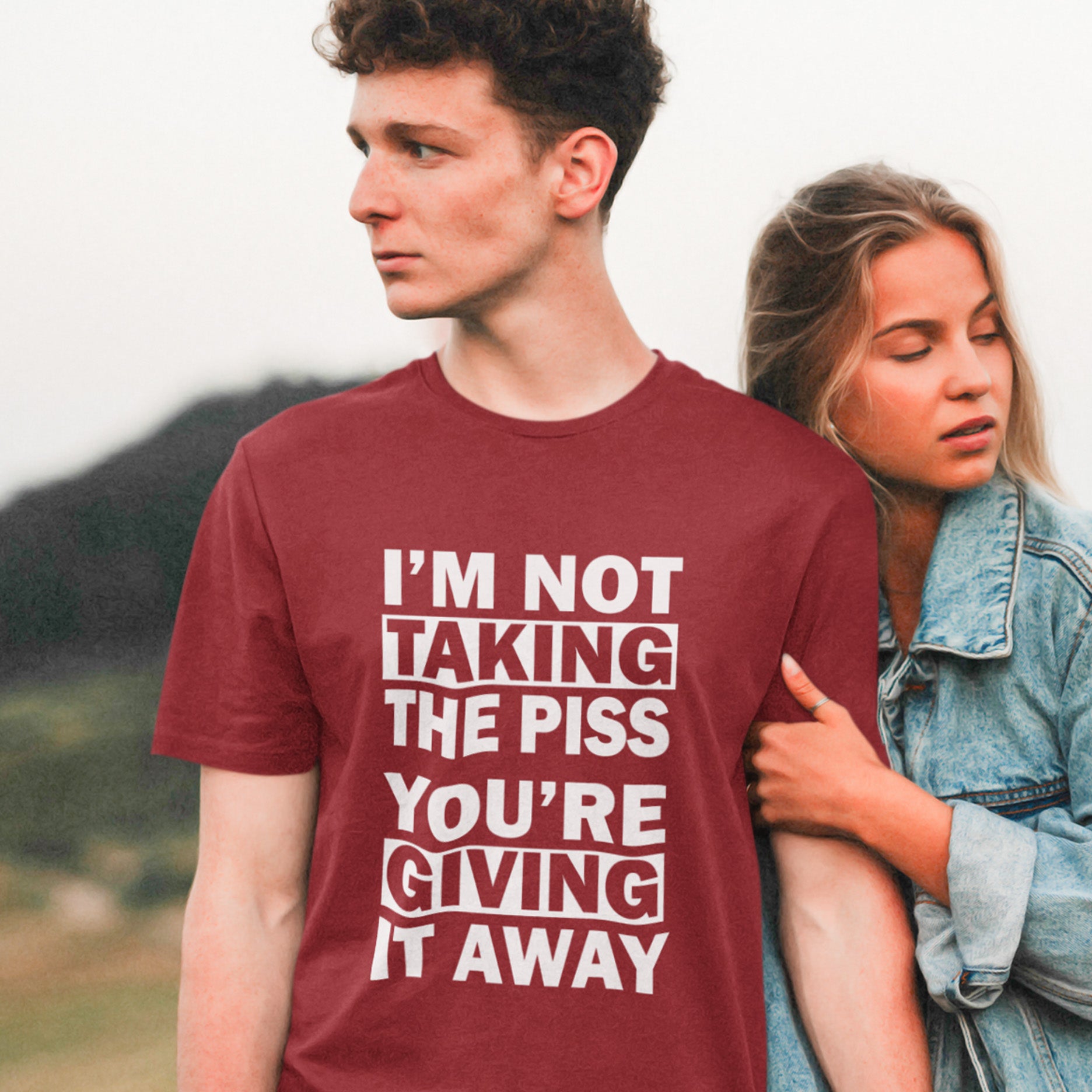 Person wearing a burgundy t-shirt with humorous text, standing outdoors with a blurred background. A clever slogan t shirt design suggesting some people just set themselves up to be laughed at. Light hearted banter between friends , "No offence intended mate". Made from 100% organic ring-spun cotton, this sarcastic slogan t shirt is unisex, high-quality, super comfy, and best of all, eco-friendly.