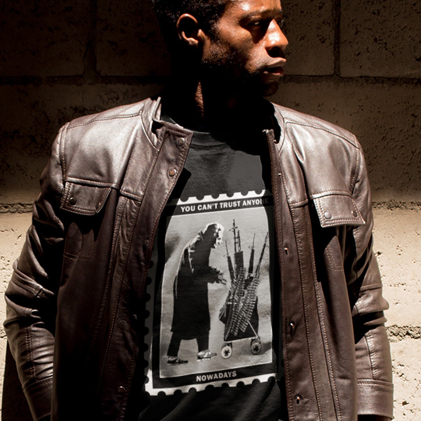 Person wearing a leather jacket and graphic t-shirt with text and images. A Banksy style street art stencil t-shirt displaying a humorous view of how careful you have to be living in a culture of fear when you come from a more trusting generation. Made from 100% organic ring-spun cotton, this street art t-shirt is unisex, high-quality, super comfy, and best of all, eco-friendly.