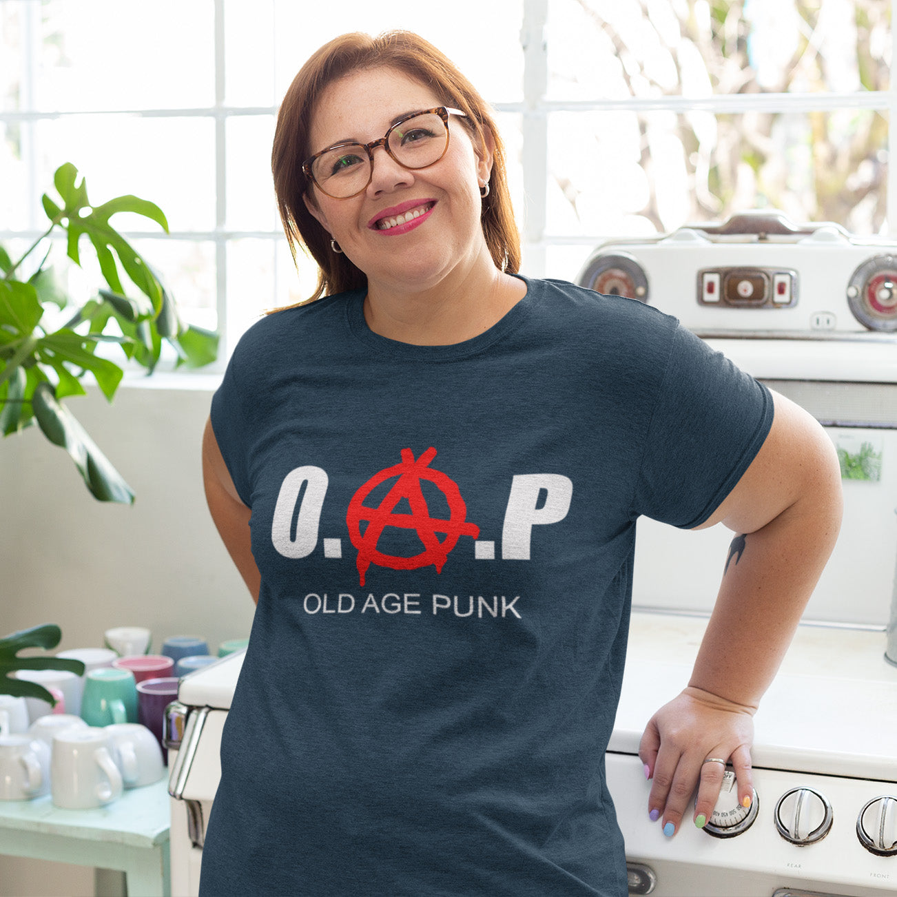 Woman wearing a French navy blue t-shirt with 'O.A.P. OLD AGE PUNK' design in a kitchen. A funny nonconformist t-shirt for all you oldies out there that still don't agree with the system, or if you have a parent or grandparent with an attitude, this is a great sarcastic t-shirt present. Made from 100% organic ring-spun cotton, this punk rocker t-shirt is unisex, high-quality, super comfy, and best of all, eco-friendly.