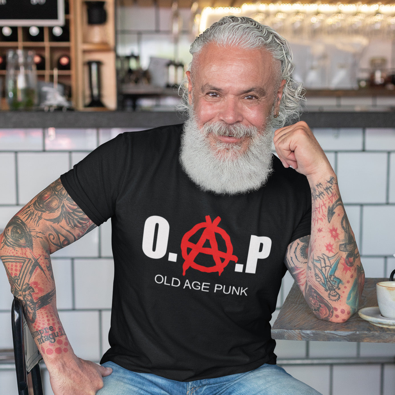 Man wearing a black t-shirt with 'O.A.P. Old Age Punk' design in a casual setting. A funny nonconformist t-shirt for all you oldies out there that still don't agree with the system, or if you have a parent or grandparent with an attitude, this is a great sarcastic t-shirt present. Made from 100% organic ring-spun cotton, this punk rocker t-shirt is unisex, high-quality, super comfy, and best of all, eco-friendly.
