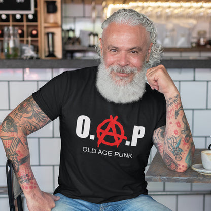 Man wearing a black t-shirt with 'O.A.P. Old Age Punk' design in a casual setting. A funny nonconformist t-shirt for all you oldies out there that still don't agree with the system, or if you have a parent or grandparent with an attitude, this is a great sarcastic t-shirt present. Made from 100% organic ring-spun cotton, this punk rocker t-shirt is unisex, high-quality, super comfy, and best of all, eco-friendly.