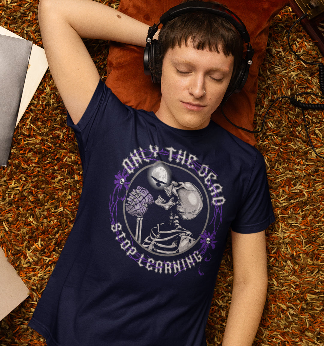 Person wearing a navy blue t-shirt with a graphic design, lying on a textured surface. These thought provoking t shirts highlight our laziness in learning. Education is a life long experience that evolves the species. When schooling ends the real learning starts. Learning is for life, unless your brain has died on you. Made from 100% organic ring-spun cotton, this counter culture t shirt is unisex, high quality, super comfy, and best of all, eco-friendly.