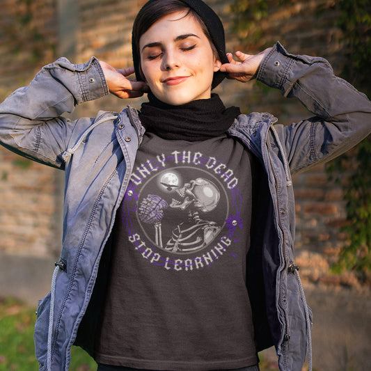 Person wearing a dark t-shirt with a graphic design and text, standing outdoors. These thought provoking t shirts highlight our laziness in learning. Education is a life long experience that evolves the species. When schooling ends the real learning starts. Learning is for life, unless your brain has died on you. Made from 100% organic ring-spun cotton, this counter culture t shirt is unisex, high quality, super comfy, and best of all, eco-friendly.