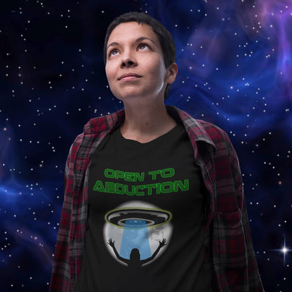 Person wearing a t-shirt with 'Open to Abduction' design against a starry space background. A funny alien abduction t-shirt design for those who feel a distance forming between them and the rest of the human race. Made from 100% organic ring-spun cotton, this alien abduction t-shirt is unisex, high-quality, super comfy, and best of all, eco-friendly.