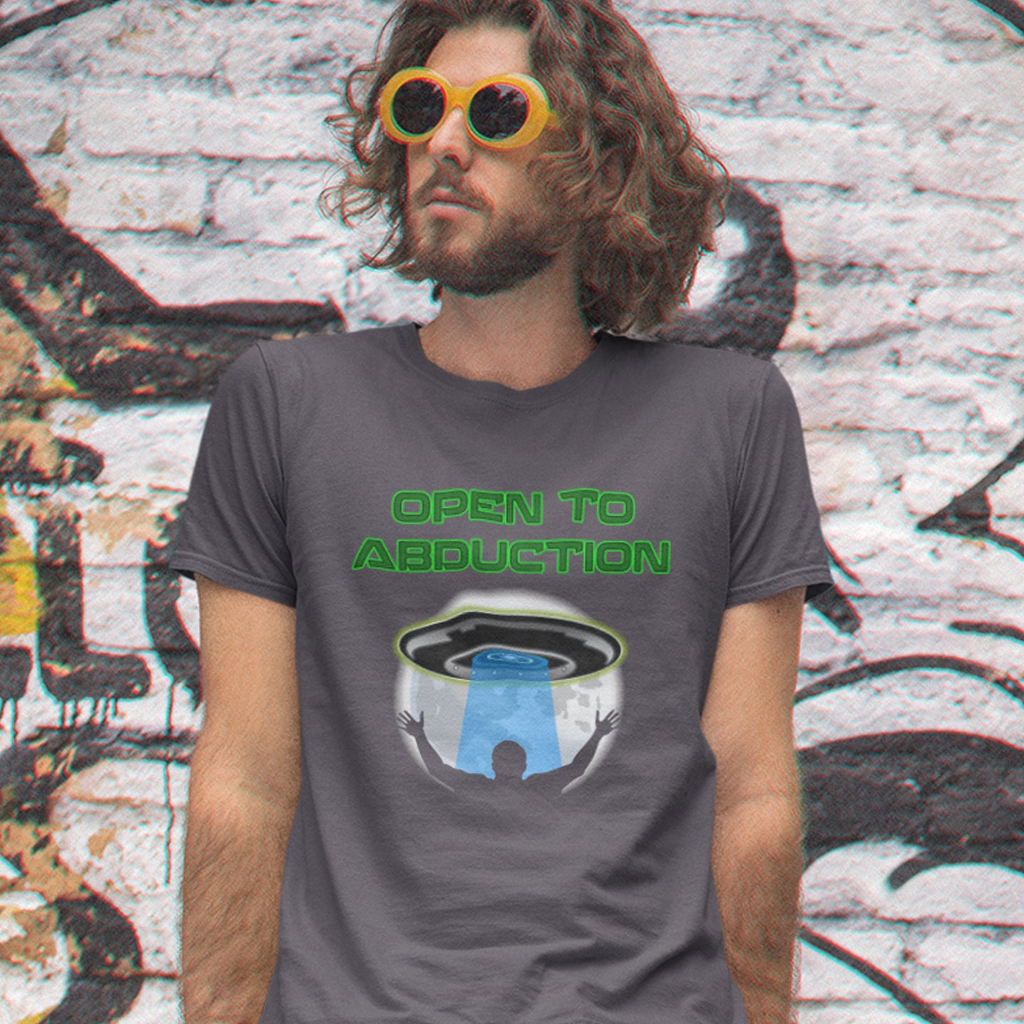 Person wearing a t-shirt with 'Open to Abduction' graphic design in front of a graffiti-covered wall. A funny alien abduction t-shirt design for those who feel a distance forming between them and the rest of the human race, and are not too impressed with our lack of effort to save the planet. This design depicts a man open to abduction. Made from 100% organic ring-spun cotton, this witty alien abduction t-shirt is unisex, high-quality, super comfy, and best of all, eco-friendly.