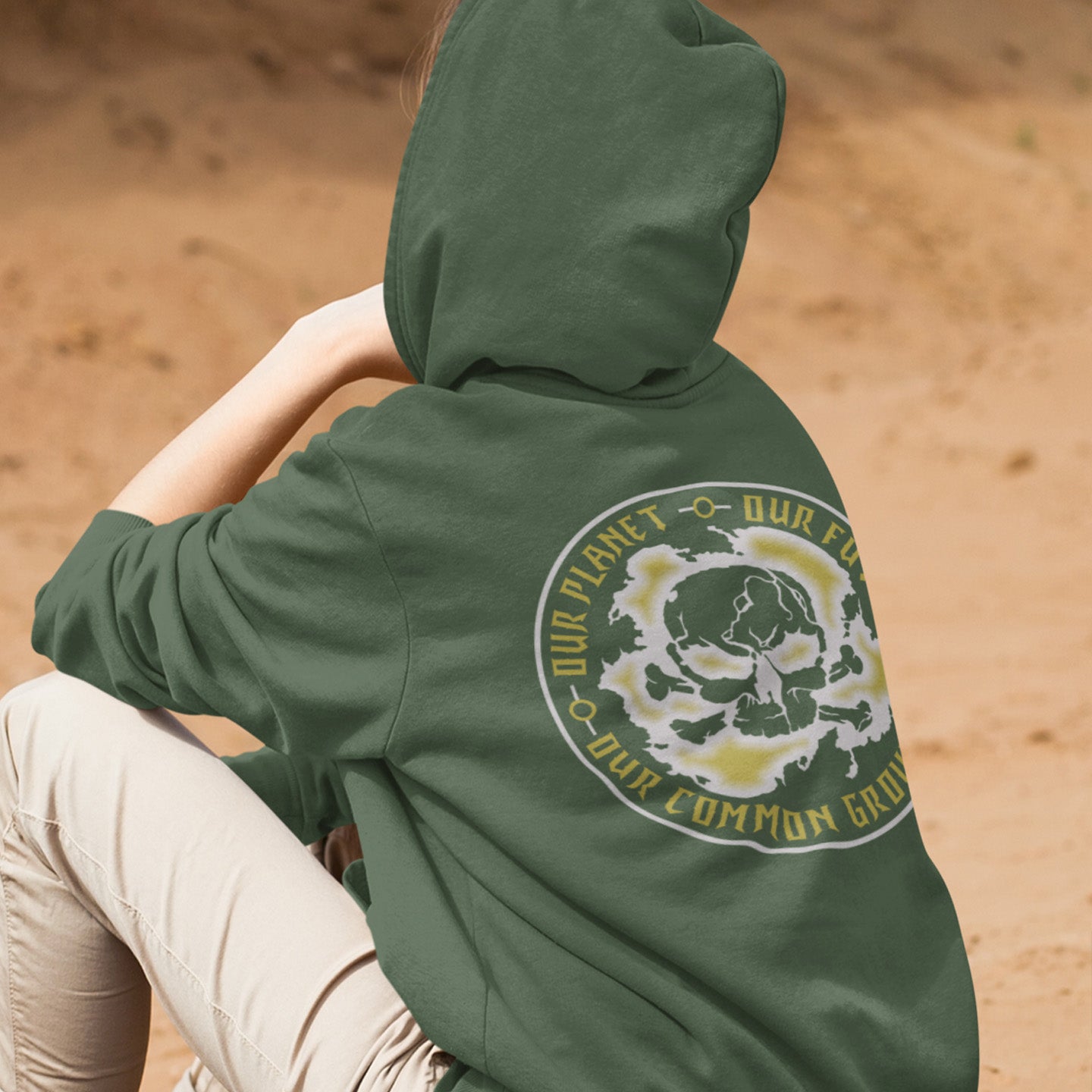 Person wearing a green hoodie with a circular design and text on a sandy background. An environmental concern hoodie for nature lovers who want to save the planet. Planet welfare should be something we can all agree on. Comfortable and practical. It's extra soft and has a convenient front pouch pocket. Made from organic cotton and recycled polyester, this environmental awareness hoodie is a great eco-friendly choice.