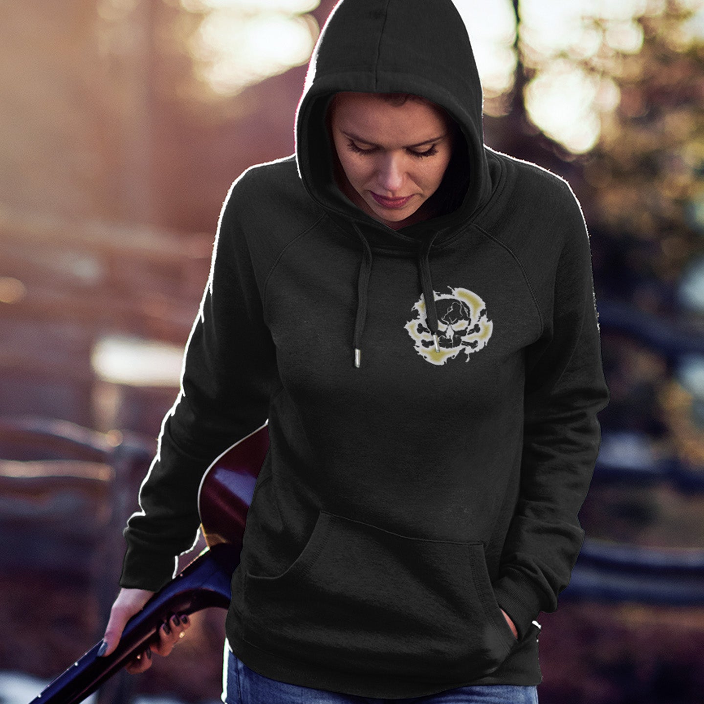 Person wearing a black hoodie with a logo, holding a guitar outdoors. An environmental concern hoodie for nature lovers who want to save the planet. Planet welfare should be something we can all agree on. Comfortable and practical. It's extra soft and has a convenient front pouch pocket. Made from organic cotton and recycled polyester, this environmental awareness hoodie is a great eco-friendly choice.