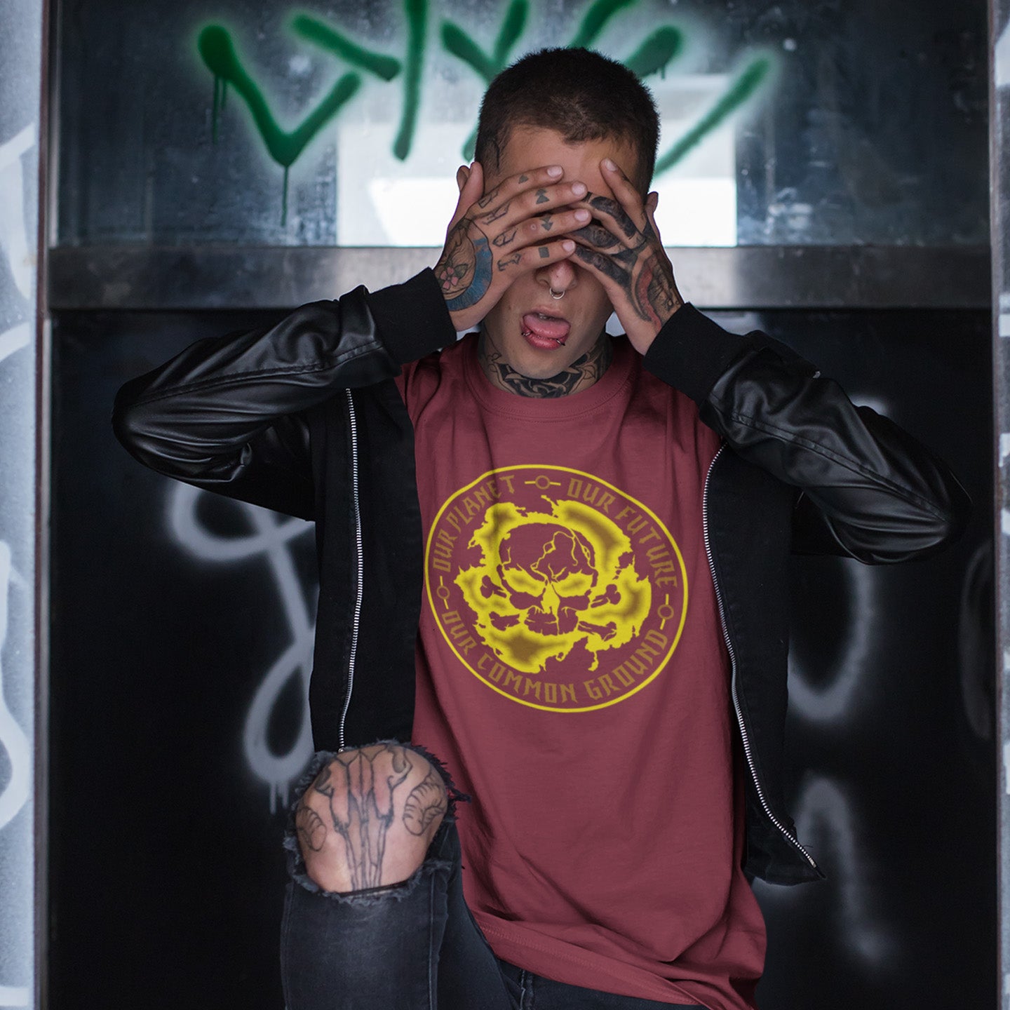 Person wearing a burgundy t-shirt with a yellow graphic design, covering their face with tattooed hands against a graffiti-covered wall. A save the planet t shirt for nature lovers who have environmental concern. Planet welfare should be something we can all agree on. Made from 100% organic ring-spun cotton, this save the Earth t shirt is unisex, high-quality, super comfy, and best of all, eco-friendly. Yellow design.