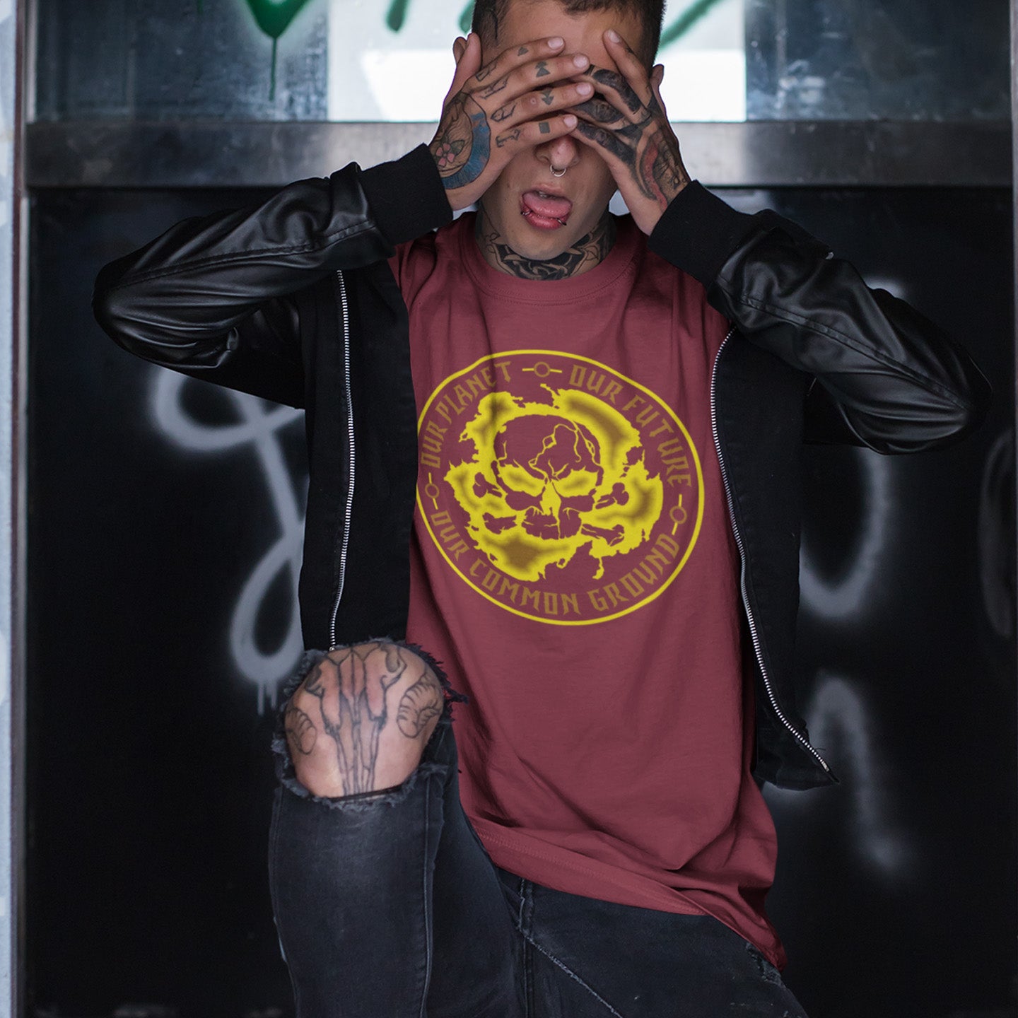 Person wearing a maroon t-shirt with a yellow graphic design, sitting against a dark background. An environmental concern t-shirt for nature lovers who want to save the planet. Planet welfare should be something we can all agree on. Made from 100% organic ring-spun cotton, this climate concern t-shirt is unisex, high-quality, super comfy, and best of all, eco-friendly. yellow design.