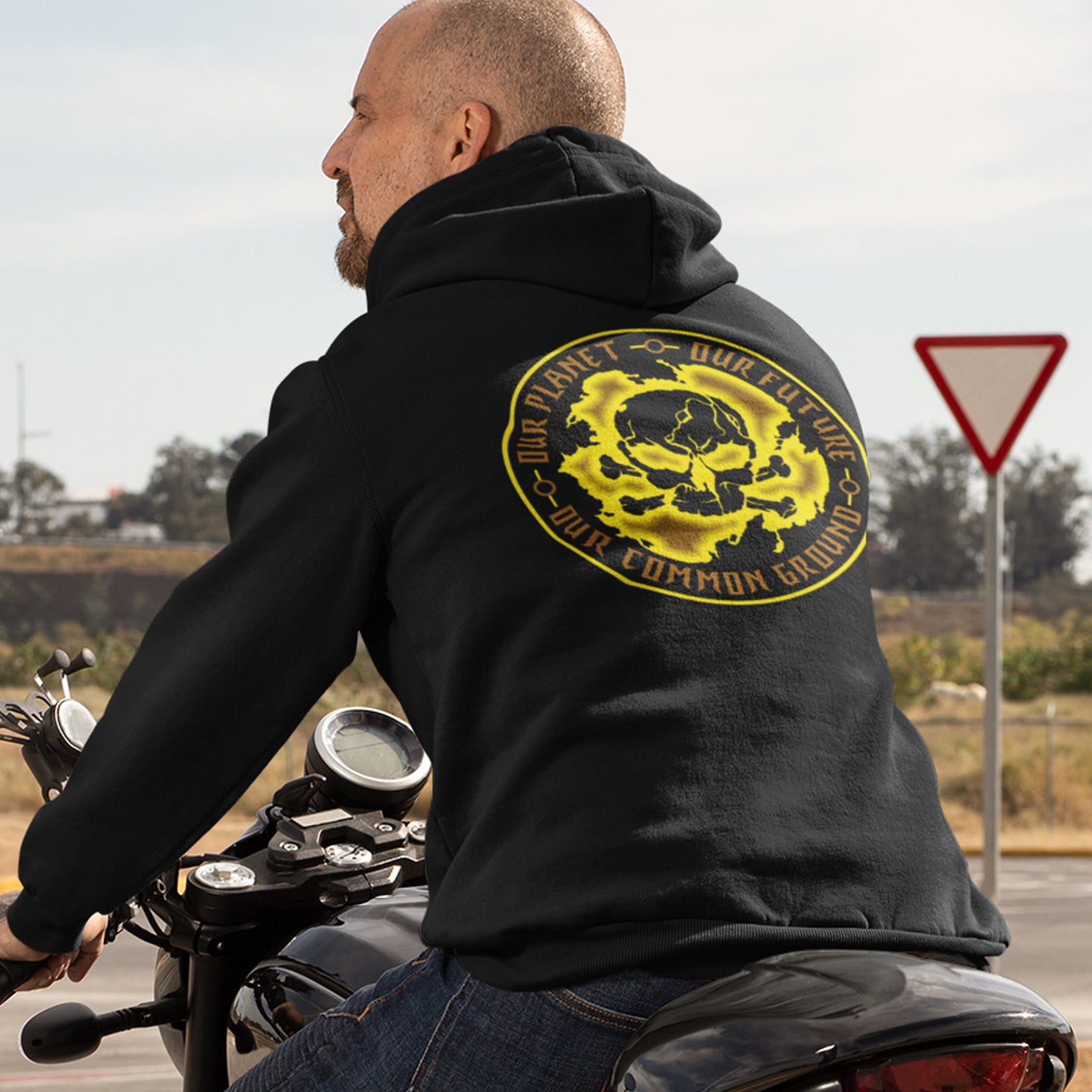 Man on a motorcycle wearing a black hoodie with a yellow graphic design. An environmental concern hoodie in a yellow design, for nature lovers who want to save the planet. Planet welfare should be something we can all agree on. Comfortable and practical. It's extra soft and has a convenient front pouch pocket. Made from organic cotton and recycled polyester, this environmental awareness hoodie is a great eco-friendly choice.