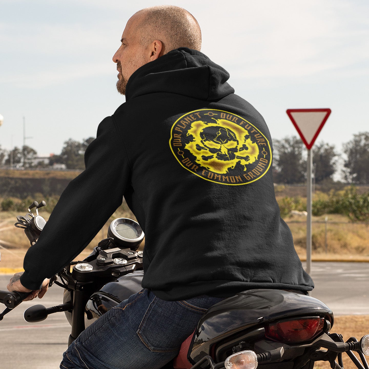 Man on a motorcycle wearing a black hoodie with a yellow and black graphic design. A save the Earth hoodie in a yellow design, for nature lovers who have environmental concern. Planet welfare should be something we can all agree on. Comfortable and practical. It's extra soft and has a convenient front pouch pocket. Made from organic cotton and recycled polyester, this save the world hoodie is a great eco-friendly choice.