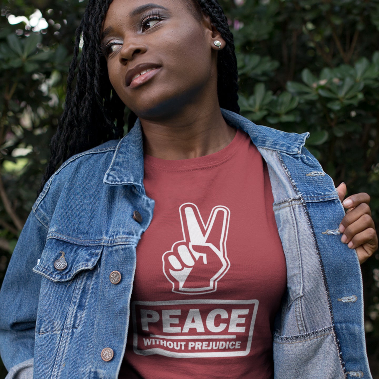 Woman wearing a burgundy t-shirt with a peace sign and 'Peace Without Prejudice' text, standing outdoors. This anti racism t-shirt highlights how equality is a key component of peace on Earth. For us to live in harmony we need to improve our emotional intelligence and acceptance of differences, especially when it comes to racial issues. Made from 100% organic ring-spun cotton, this anti racist t shirt is unisex, high-quality, super comfy, and best of all, eco-friendly.