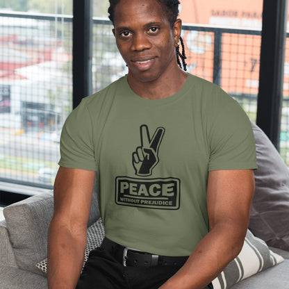 A man sitting on the arm of a chair, wearing a khaki t-shirt with a black printed peace sign and "Peace without prejudice" written underneath.
