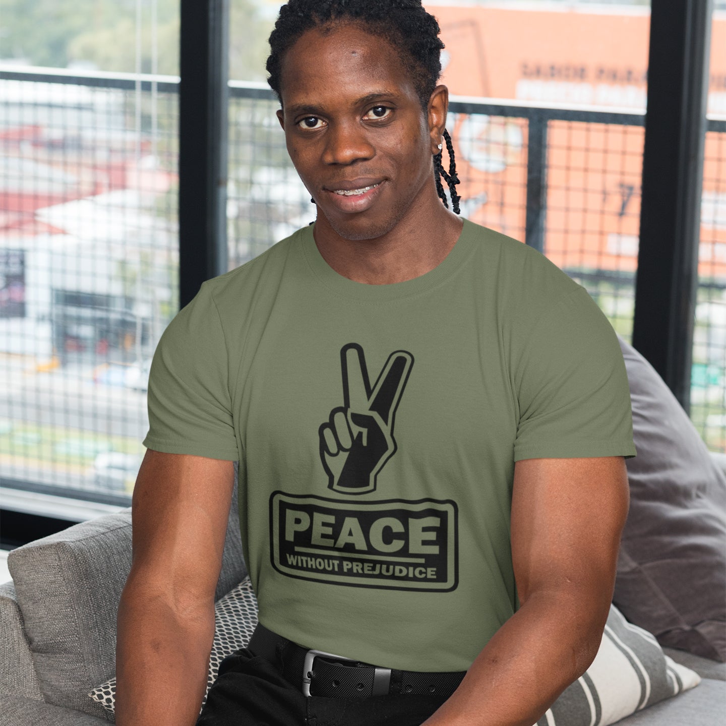 Person wearing a khaki t-shirt with a peace symbol and 'Peace Without Prejudice' text. This anti racism t-shirt highlights how equality is a key component of peace on Earth. For us to live in harmony we need to improve our emotional intelligence and acceptance of differences, especially when it comes to racial issues. Made from 100% organic ring-spun cotton, this anti racist t shirt is unisex, high-quality, super comfy, and best of all, eco-friendly.