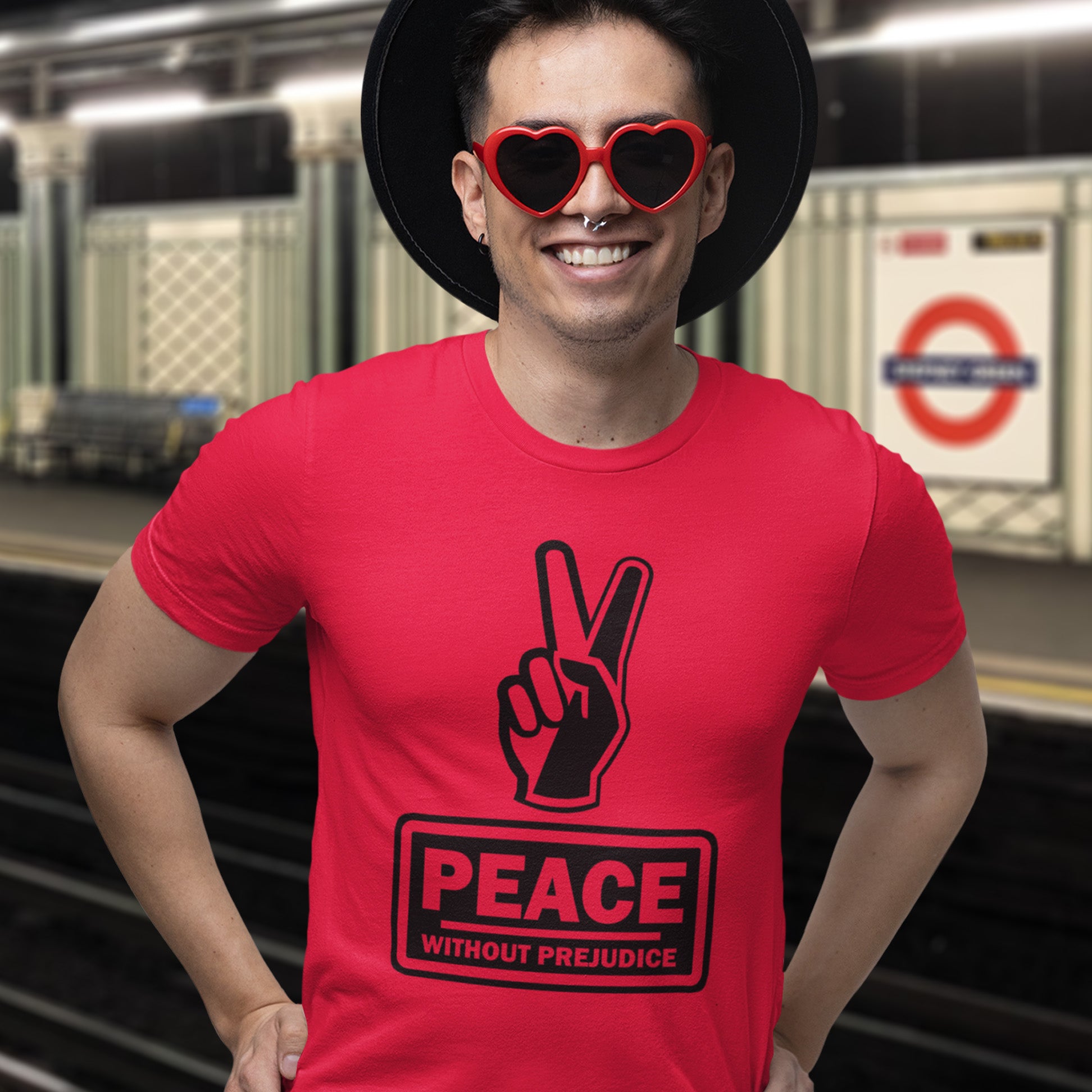 Person wearing a red t-shirt with a peace symbol and 'Peace Without Prejudice' text, standing in a subway station. This anti racism t-shirt highlights how equality is a key component of peace on Earth. For us to live in harmony we need to improve our emotional intelligence and acceptance of differences, especially when it comes to racial issues. Made from 100% organic ring-spun cotton, this anti racist t shirt is unisex, high-quality, super comfy, and best of all, eco-friendly.