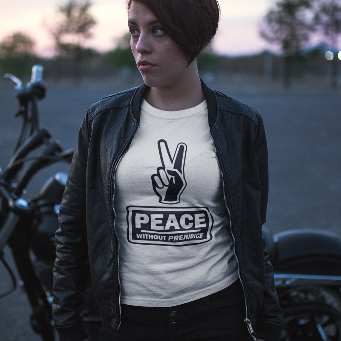 Person wearing a t-shirt with 'Peace Without Prejudice' design, standing next to a motorcycle. This anti racism t-shirt highlights how equality is a key component of peace on Earth. For us to live in harmony we need to improve our emotional intelligence and acceptance of differences, especially when it comes to racial issues. Made from 100% organic ring-spun cotton, this anti racist t shirt is unisex, high-quality, super comfy, and best of all, eco-friendly.