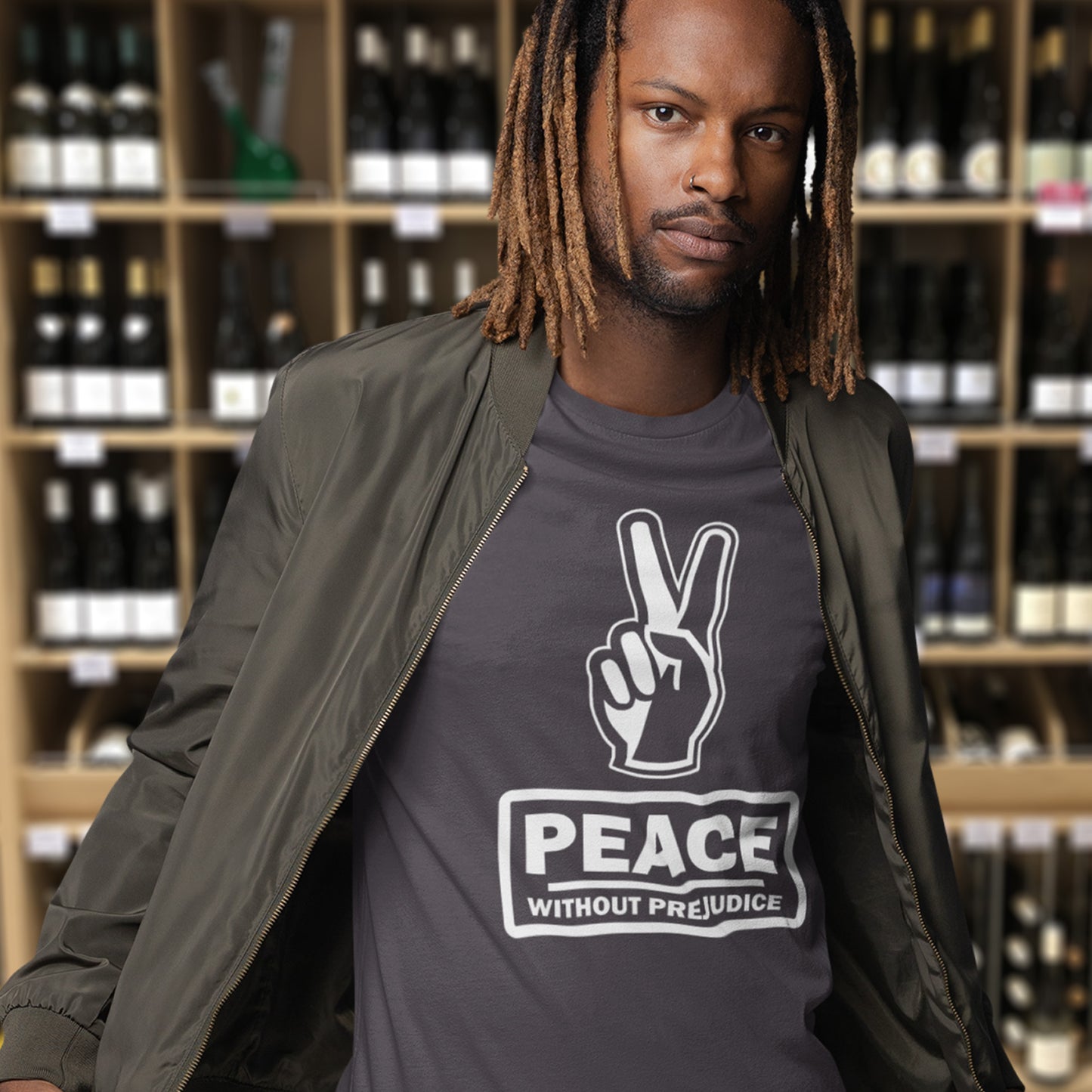 Man wearing a t-shirt with a peace sign and 'Peace Without Prejudice' text in a wine store. This anti-prejudice t-shirt highlights how equality is a key component of peace on Earth. For us to live in harmony we need to improve our emotional intelligence and acceptance of differences, especially when it comes to racial issues . Made from 100% organic ring-spun cotton, this anti racism, pro equality t-shirt is unisex, high-quality, super comfy, and best of all, eco-friendly.