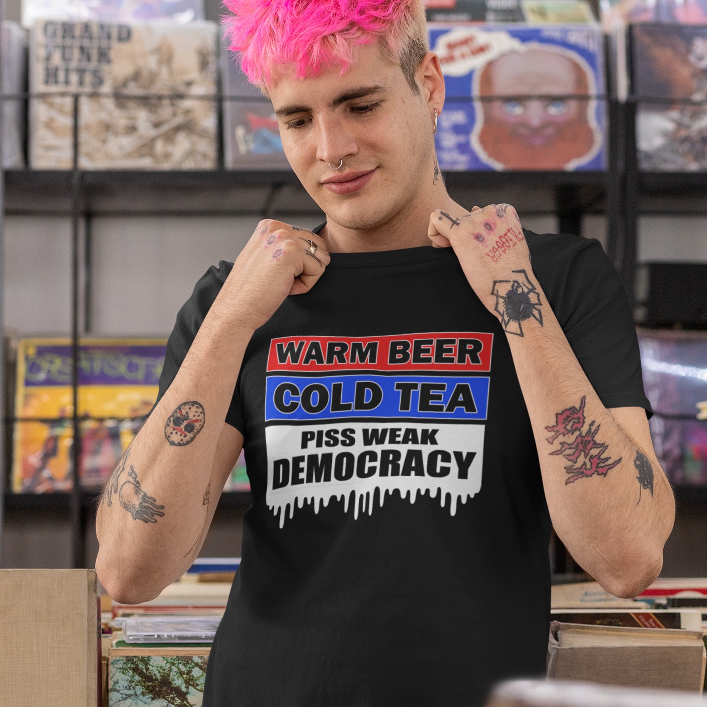 Person wearing a black t-shirt with a colourful graphic design in a record store. This anti-establishment t-shirt comes with a short poem. Warm beer, cold tea, piss weak democracy. These are the things no one wants served to them !! this unique political t-shirt design is idea for any demonstration or protest rally. Made from 100% organic ring-spun cotton, this political anti government t-shirt is unisex, high-quality, super comfy, and best of all, eco-friendly.
