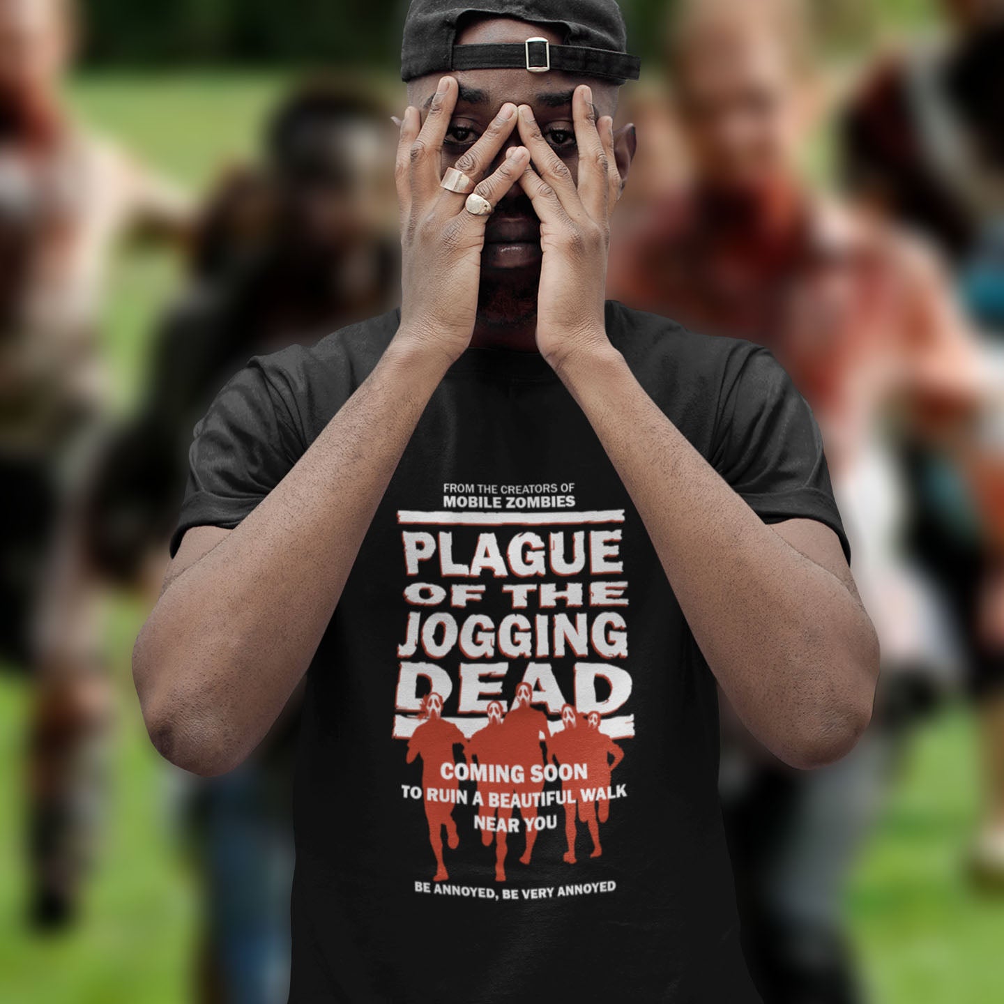 Person wearing a black t-shirt with a humorous graphic and text, standing in front of a blurred background. A satirical t-shirt about jogging in a horror movie design. Just when you thought it was safe to go out for a nice relaxing walk. Made from 100% organic ring-spun cotton, this social awareness t-shirt is unisex, high-quality, super comfy, and best of all, eco-friendly.