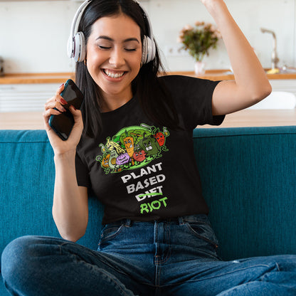 Woman enjoying music, wearing headphones, sitting on a couch, wearing a black t-shirt featuring a graphic print of a green chili pepper and a red chilli character with the text 'SPICY VEGAN' underneath.