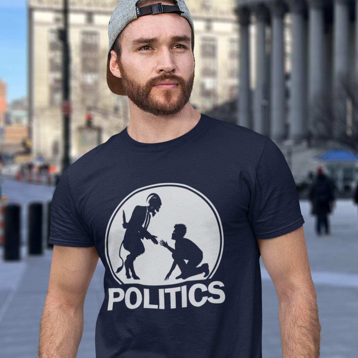 Man wearing a French navy blue t-shirt with a graphic design and the word 'POLITICS' on a city street. An anti government t shirt representing the simple inner workings of politics. Are they not stabbing the working class in the back to help the rich get richer ? Show your disapproval with this urban art t shirt. Made from 100% organic ring-spun cotton, this funny political t shirt is unisex, high-quality, super comfy, and best of all, eco-friendly.