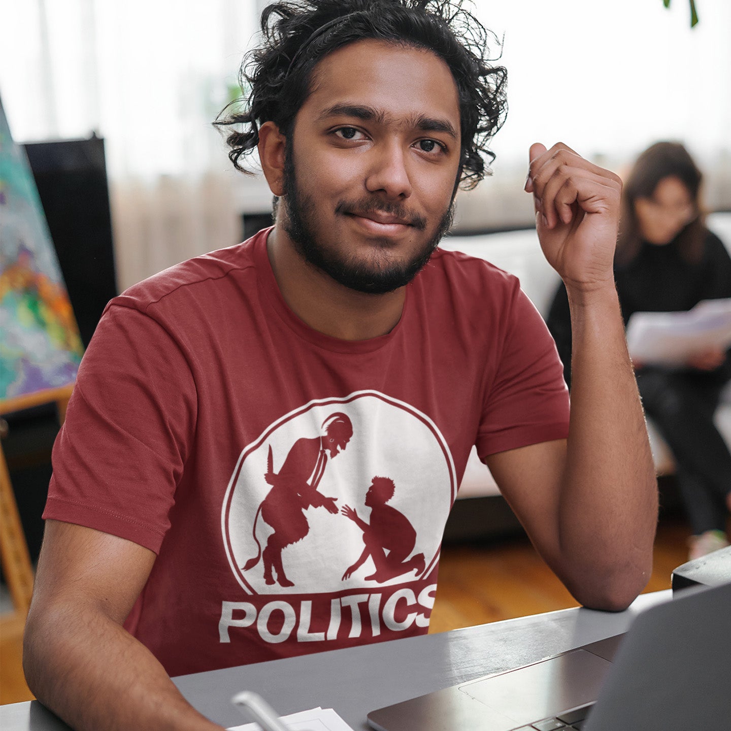 Man wearing a burgundy t-shirt with a graphic and text, sitting at a desk. An anti government t shirt representing the simple inner workings of politics. Are they not stabbing the working class in the back to help the rich get richer ? Show your disapproval with this urban art t shirt. Made from 100% organic ring-spun cotton, this funny political t shirt is unisex, high-quality, super comfy, and best of all, eco-friendly.