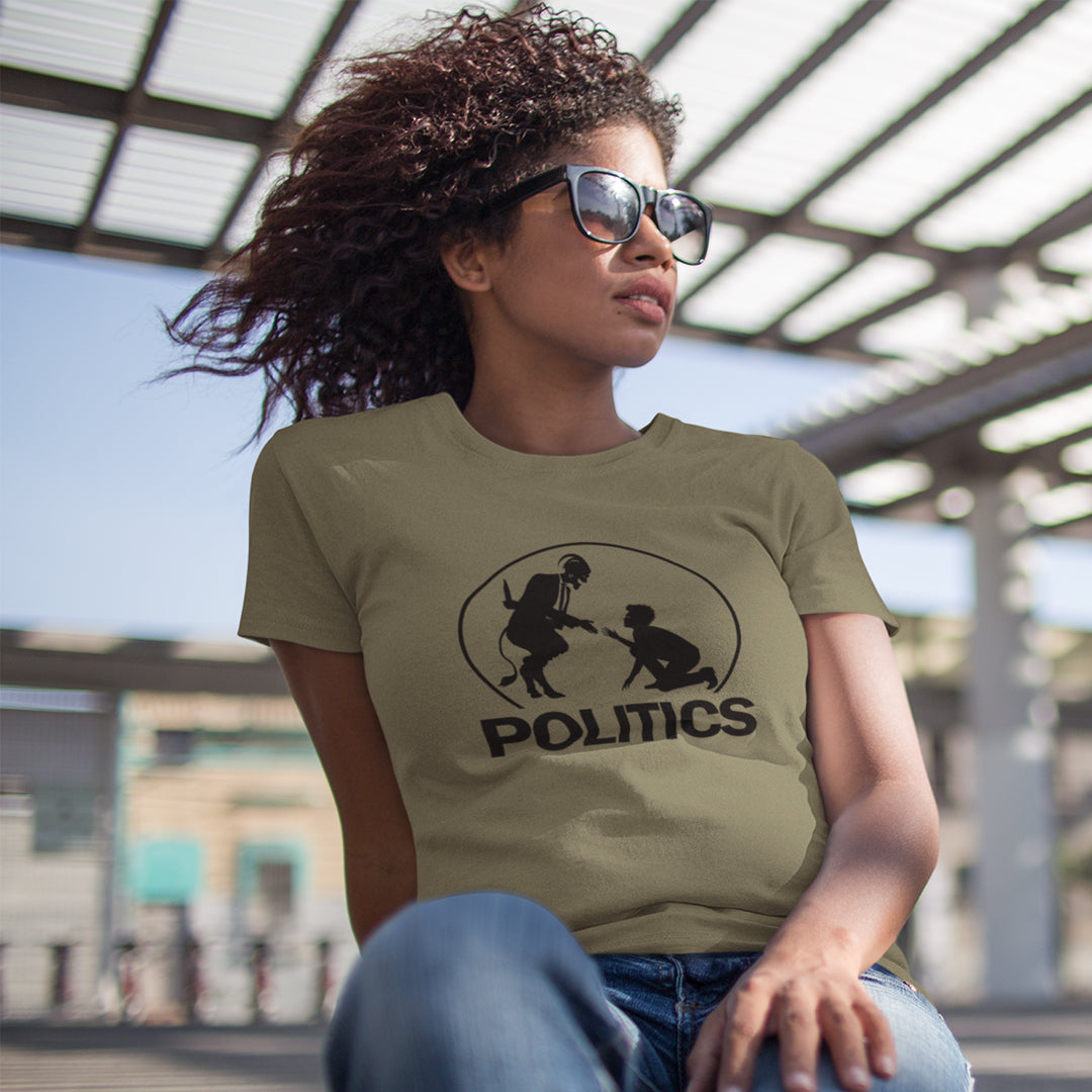 A woman in sunglasses, sitting outside wearing a khaki t-shirt  with a black graphic print on the chest. The graphic features a circular silhouette illustration of a standing figure reaching toward a kneeling figure, with the word 'POLITICS' printed in bold white capital letters underneath.