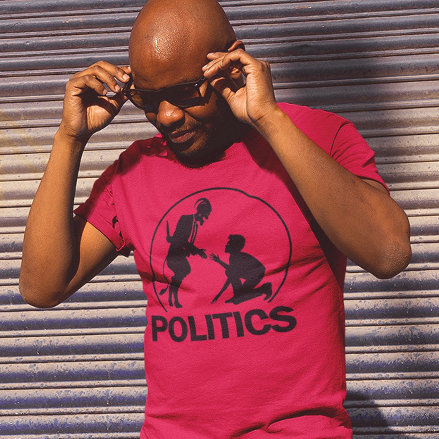 Man wearing a red t-shirt with a graphic and the word 'POLITICS' against a corrugated metal background. An anti government t shirt representing the simple inner workings of politics. Are they not stabbing the working class in the back to help the rich get richer ? Show your disapproval with this urban art t shirt. Made from 100% organic ring-spun cotton, this funny political t shirt is unisex, high-quality, super comfy, and best of all, eco-friendly.