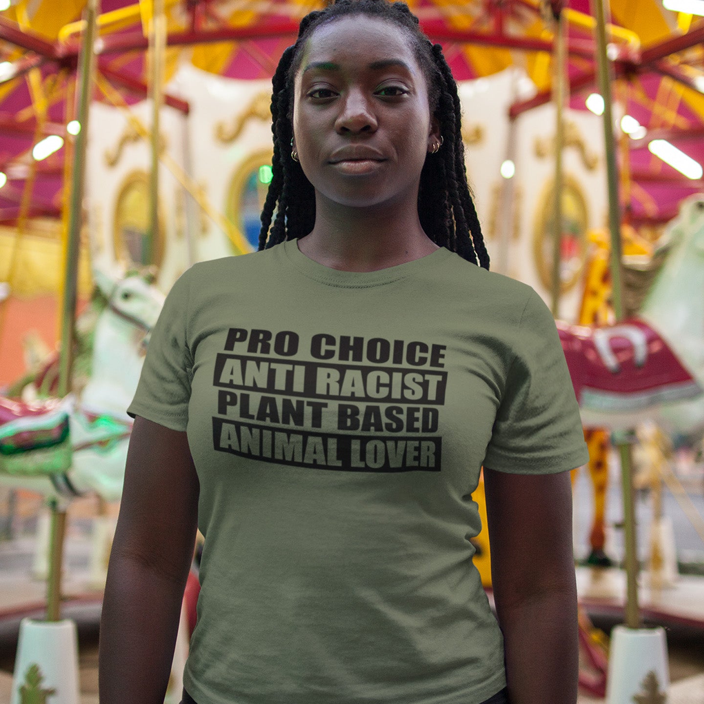 Person wearing a t-shirt with pro-choice, anti-racist, plant-based, animal lover text in front of a carousel. A plant based meat free t shirt design intertwined with Pro Choice, Anti Racism, and Animal loving, characteristics that often go together. Made from 100% organic ring-spun cotton, this dairy free t shirt is unisex, high-quality, super comfy, and best of all, eco-friendly.