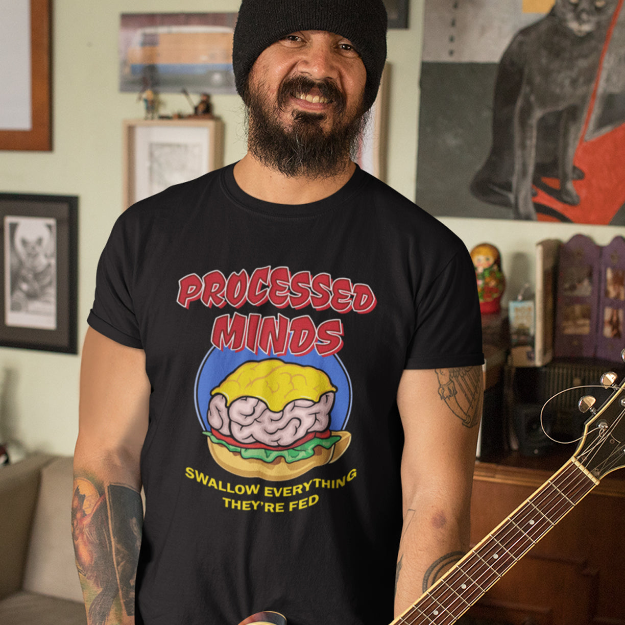 Man wearing a black t-shirt with graphic design and text, holding a guitar in a room. This sign of the times t shirt design represents the amount of influence and mental manipulation in circulation these days. Resist the brainwashing and bring back wild and organic independent thinking. Made from 100% organic ring-spun cotton, these social issues t shirts are unisex, high-quality, super comfy, and best of all, eco-friendly.